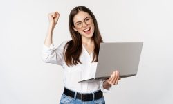 Enthusiastic office woman, businesswoman holding laptop and shouting with joy, celebrating and rejoicing, standing over white background.